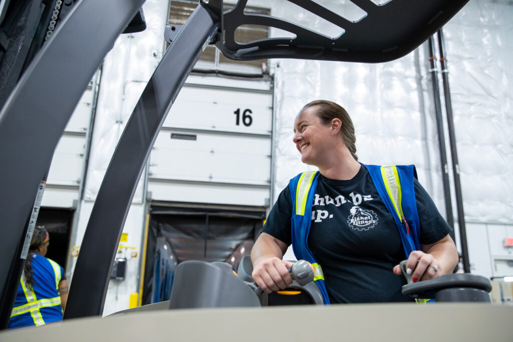 smiling woman in blue vest driving a forklift