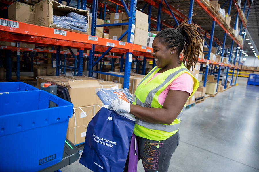 smiling woman in reflective vest bagging a product in an ecommerce fulfillment warehouse at Distribution Management